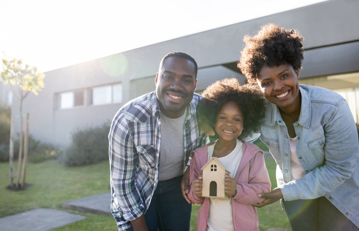 family solar installation in front of home African American family looking very happy after buying a house and smiling while holding a model - home ownership concepts